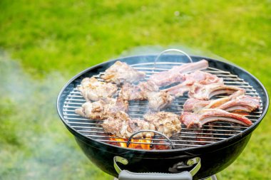 Kömür ızgarasında yeşil çimlerde pişen lezzetli etin yakın plan görüntüsü.