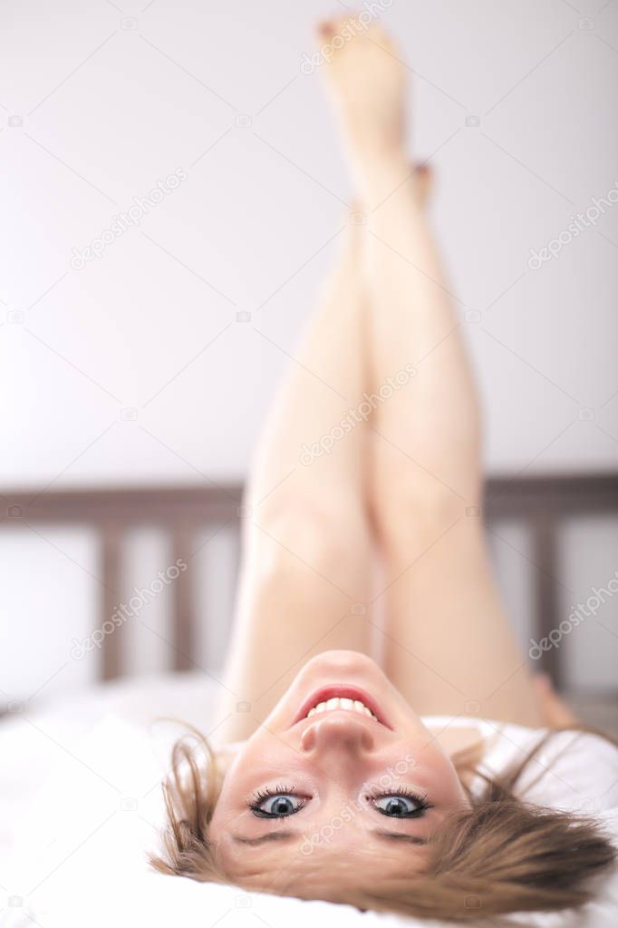 beautiful young woman lying upside down on bed and smiling at camera