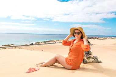 şapka ve güneş gözlüğü kumsalda oturan güzel gülümseyen genç kadın