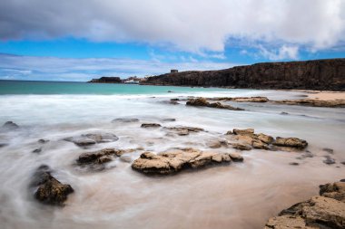 Kumlu sahili, kayalıkları ve gökyüzünde bulutları olan inanılmaz deniz manzarası.