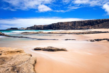 Kumlu deniz manzarası, kayalar ve mavi deniz dalgaları. 