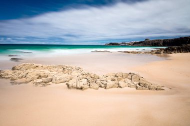 Kumlu deniz manzarası, kayalar ve mavi deniz dalgaları. 