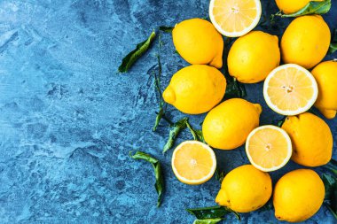 mavi zemin üzerine yeşil yaprakları ile bütünleşmiş ve yarıya sulu limon üstten görünüm   