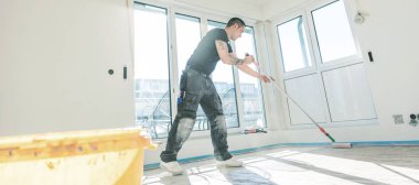 Yenileme sırasında beton zemine silindirli astar koyan işçi. Yapım aşamasında olan ev. 