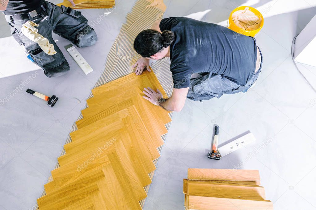 top view of male workers during process of parquet alignment 