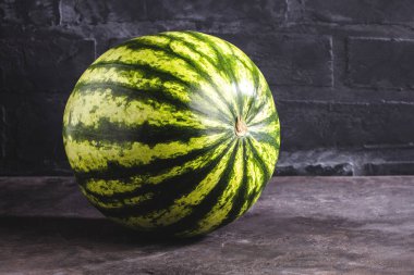 Bütün karpuz gri yüzeyi ve tuğla duvar arka plan üzerinde görmek 