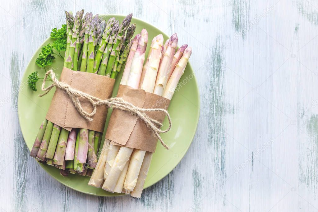 top view of tired bunches of fresh raw green and white asparagus on plate on grey surface  