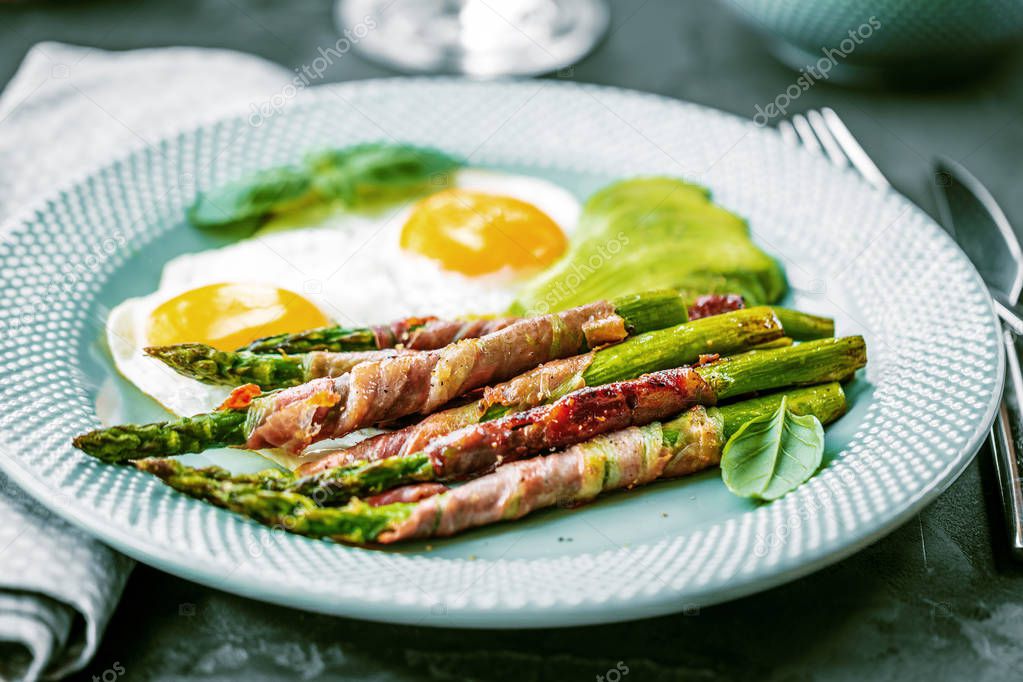 close-up view of asparagus wrapped in bacon and fried eggs on plate