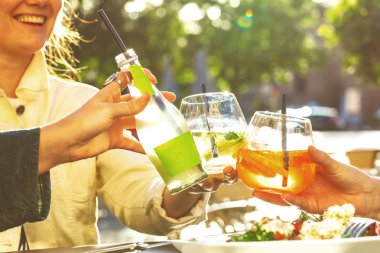 Kırpılmış bardakları tokuşturan ve dışarıda soğuk, lezzetli kokteyller içen insanları.