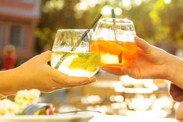 cropped shot of people clinking glasses and drinking cold tasty cocktails outdoors