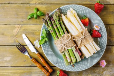 Beyaz ve yeşil kuşkonmaz ve taze çilek tabak ve çatal bıçak üzerinde ahşap masa ile üst demet