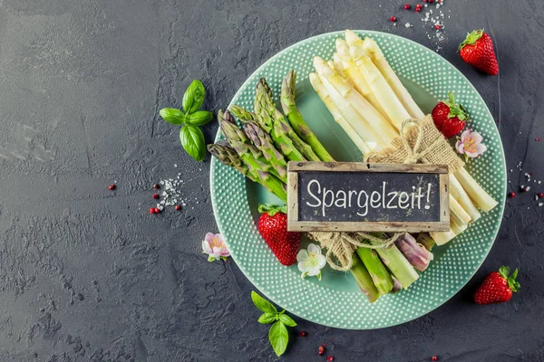 Green and white asparagus and blackboard with german text Spargelzeit or asparagus time, on a rustic wooden background