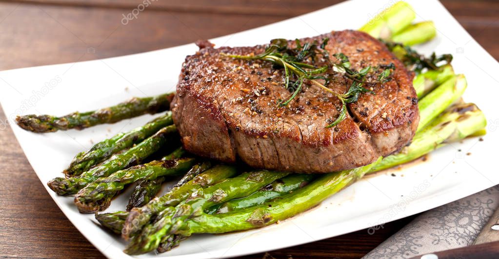 close-up view of delicious grilled steak with green asparagus and herbs on plate
