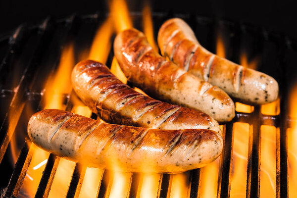 close-up view of delicious sausages cooking on grill with flame