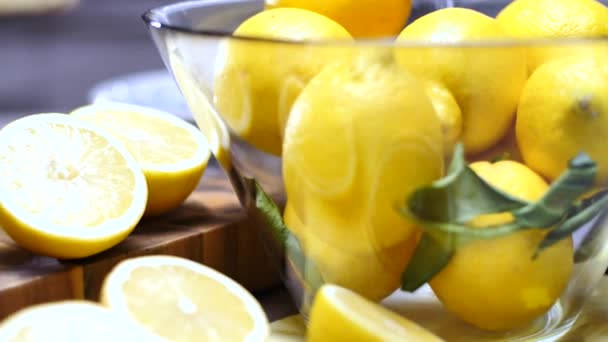 新鮮な熟したジューシーな全体と半分レモン 緑の葉とテーブルの上のガラスのボウル — ストック動画