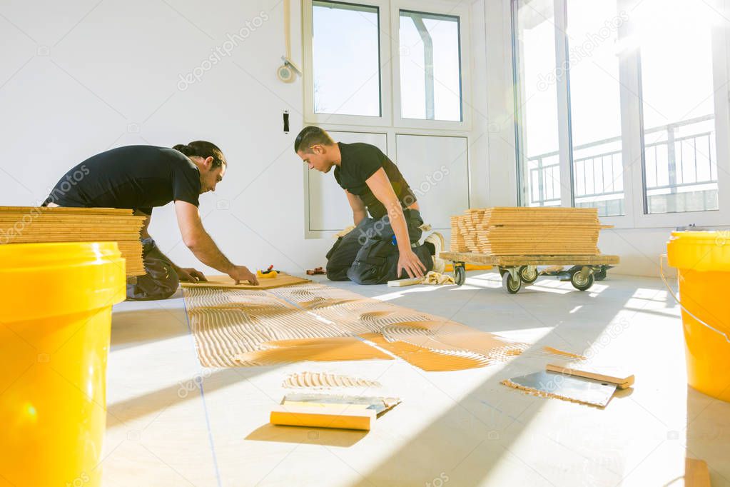 professional male workers installing oak parquet floor during home improvement  
