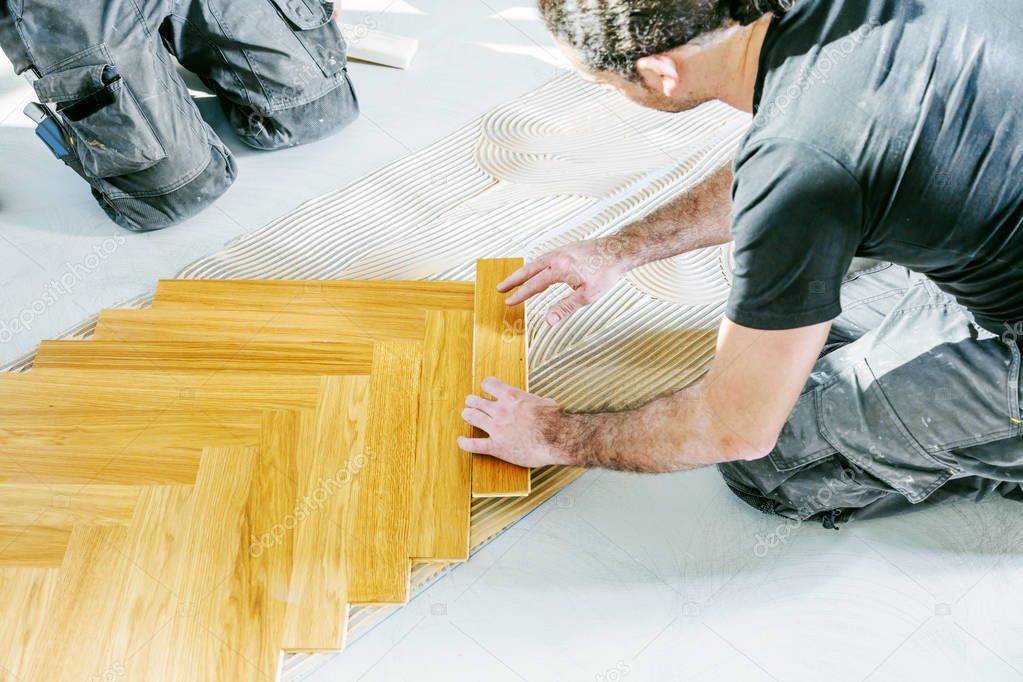 cropped shot of workers installing oak parquet floor during home improvement  