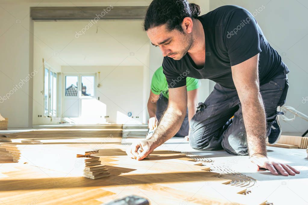 professional male workers installing oak parquet floor during home improvement  