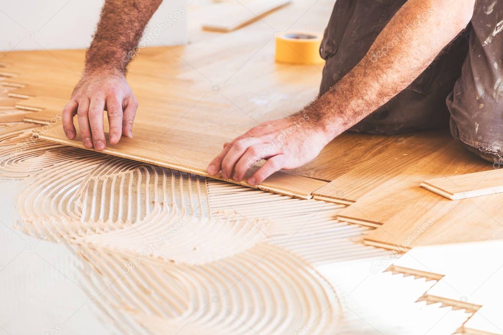 male worker varnishing oak parquet floor during home improvement