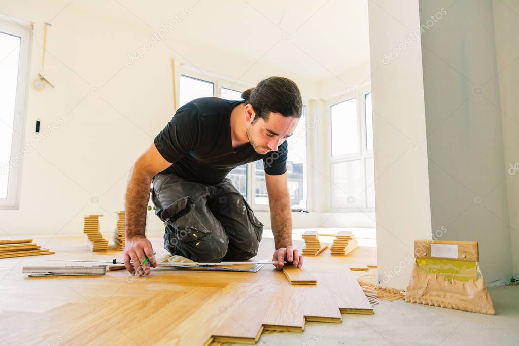 male worker varnishing oak parquet floor during home improvement