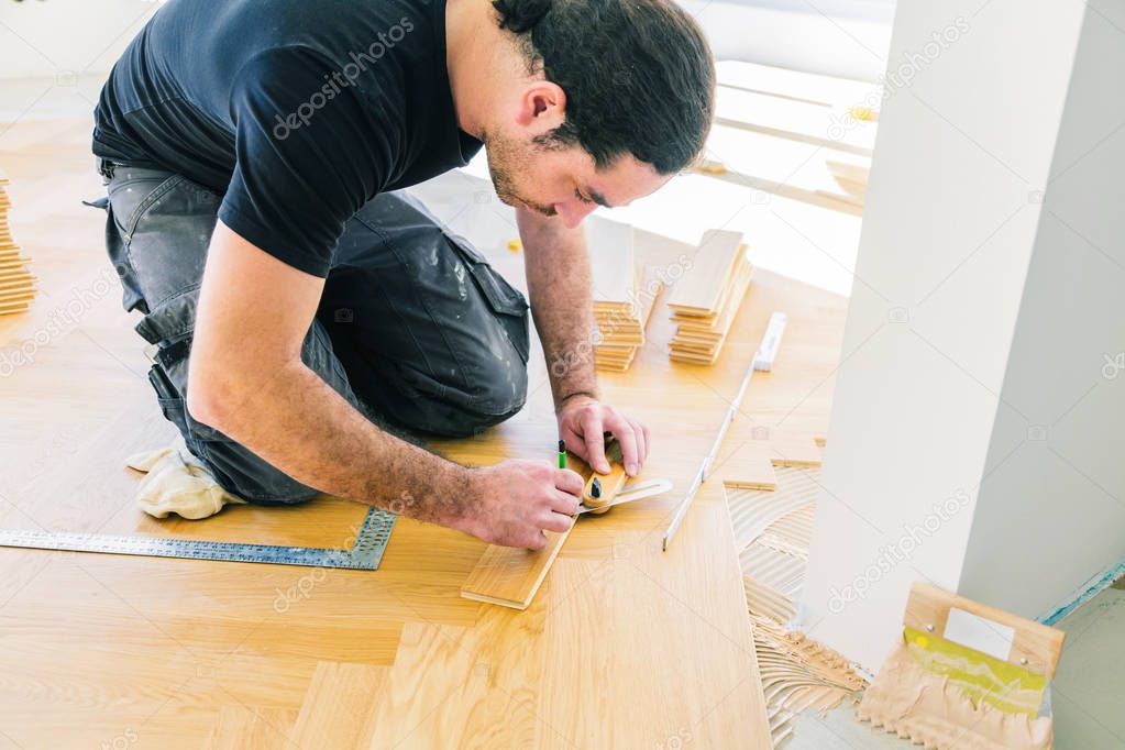 man varnishing oak parquet floor during home improvement