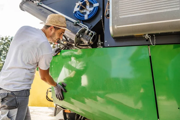 mechanic repairing the yellow and green combine harvester in the farm yard.