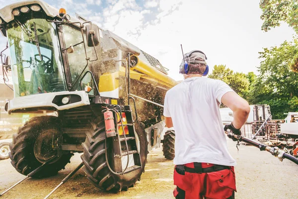 mechanic repairing the yellow and green combine harvester in the farm yard.