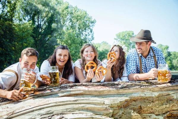 バイエルンの衣装でビールを飲み屋外でプレッツェルを食べる幸せな友人 — ストック写真