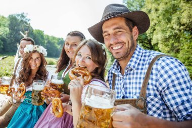 Bavyera kostümleri beş genç arkadaş bira bardakları tutan ve açık kraker yeme, oktoberfest kavramı