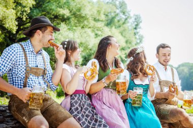 Bavyera kostümleri beş genç arkadaş bira bardakları tutan ve açık kraker yeme, oktoberfest kavramı