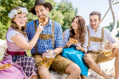 Bavyera kostümlü mutlu arkadaşlar bira içip dışarıda simit yiyorlar.