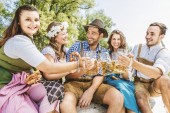 Fröhliche Freunde in bayerischen Trachten trinken Bier und essen Brezeln im Freien