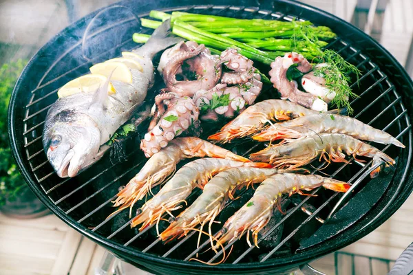 delicious prawns, fish, octopus, oysters with asparagus and herbs cooking on grill
