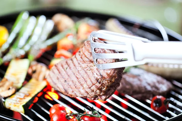 グリルの上に美味しいステーキとトングのクローズアップビュー 選択的な焦点 — ストック写真