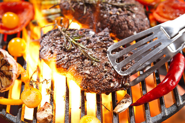 Крупный план вкусных стейков с розмарином, помидорами черри и чесноком на гриле
