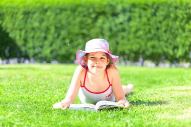 sevimli mutlu çocuk kitap ile çim üzerinde yatan ve yaz günü kamera gülümseyerek 