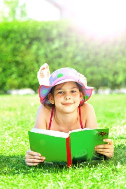 sevimli mutlu çocuk kitap ile çim üzerinde yatan ve yaz günü kamera gülümseyerek