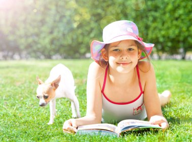 kitap ve köpek ile çim üzerinde yatan sevimli gülümseyen çocuk 