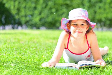 kitap ile çim üzerinde yatan ve kameraya gülümseyen sevimli çocuk