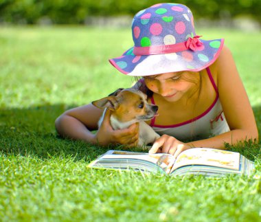 köpek ve okuma kitabı ile çim üzerinde yatan sevimli gülümseyen çocuk  