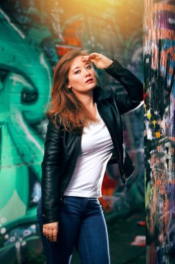 Deri ceketli baştan çıkarıcı genç kadın renkli duvar yazılarına poz veriyor. 