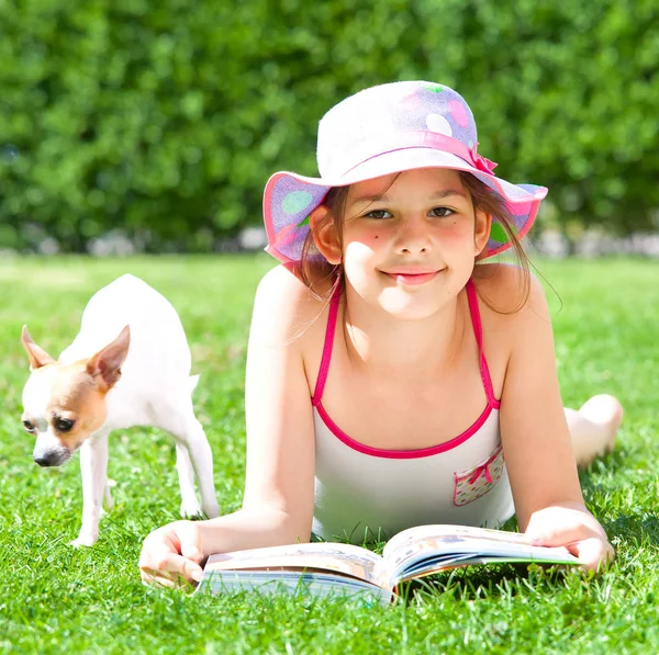 cute happy child lying on grass with book and dog and smiling at camera at summer day