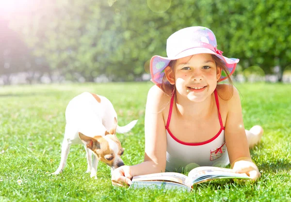adorable smiling child lying on grass with book and dog
