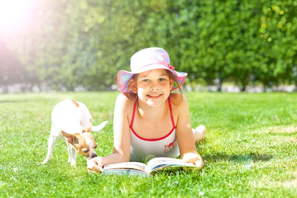 可爱的快乐的孩子躺在草地上与书和狗 并微笑着在相机在夏日 — 图库照片#
