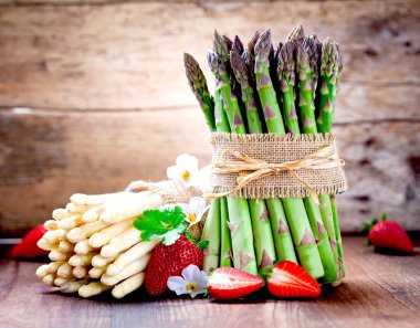 taze kuşkonmaz, çiçek ve ahşap masa üzerinde olgun çilek demet  