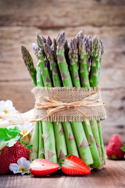 ahşap masa üzerinde taze olgun yeşil kuşkonmaz, beyaz çiçekler ve kırmızı çilek yakından görmek 