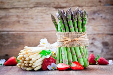 taze olgun yeşil ve beyaz kuşkonmaz, beyaz çiçekler ve ahşap masa üzerinde kırmızı çilek demet  