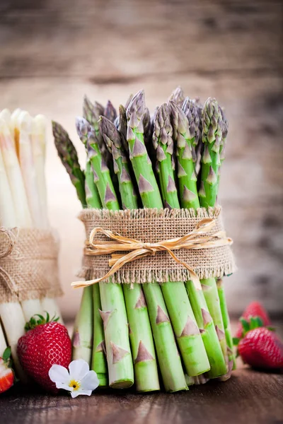 bunches of fresh green and white asparagus and ripe strawberries on wooden table