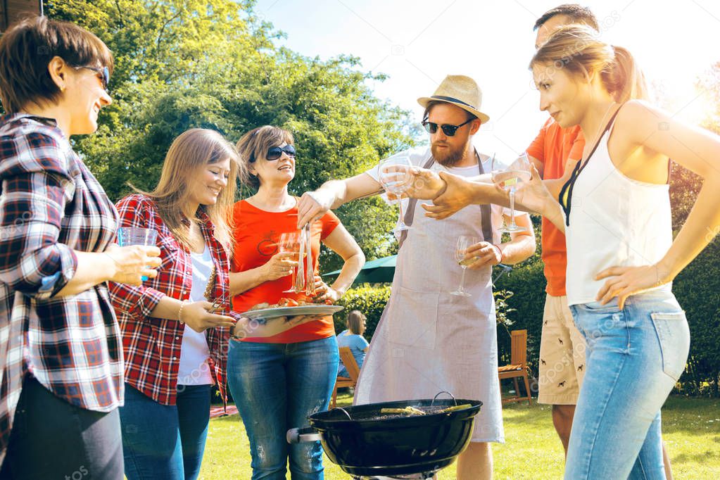 low angle view of friends cooking barbecue and drinking beverages in backyard 