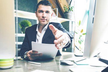 kağıtları el ulaşan ve ofiste kamera gülümseyen yakışıklı genç işadamı   